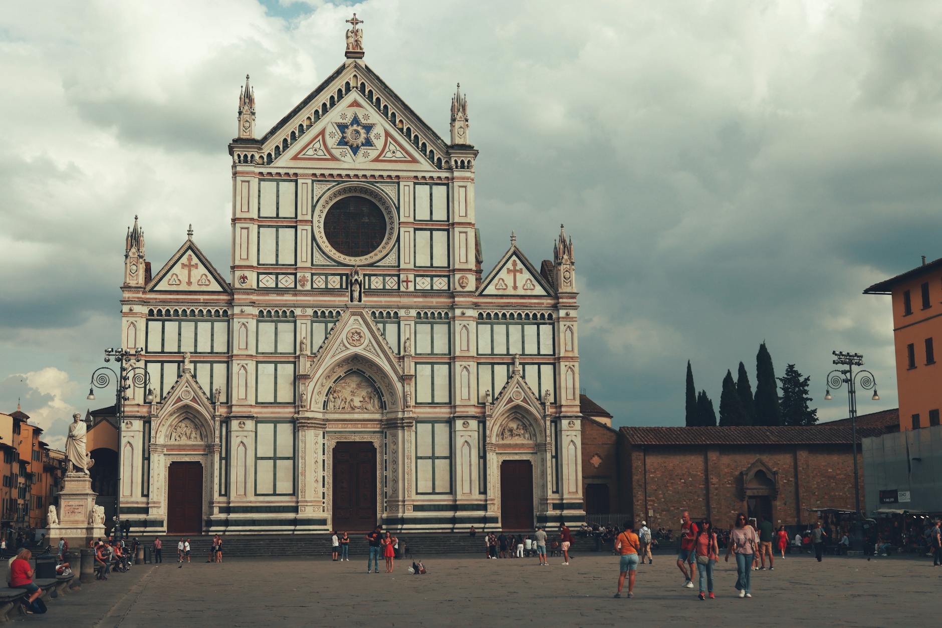 Gothic facade of Santa Croce Basilica in Florence's historic square with tourists.