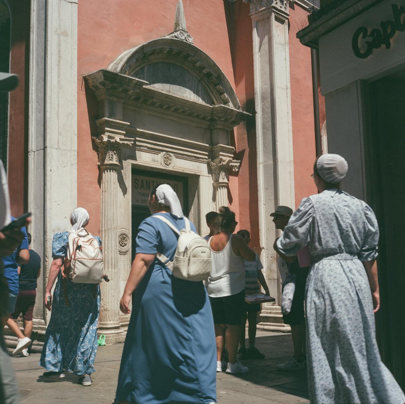 A diverse group of people gathered outside a historic church in Venice, Italy.