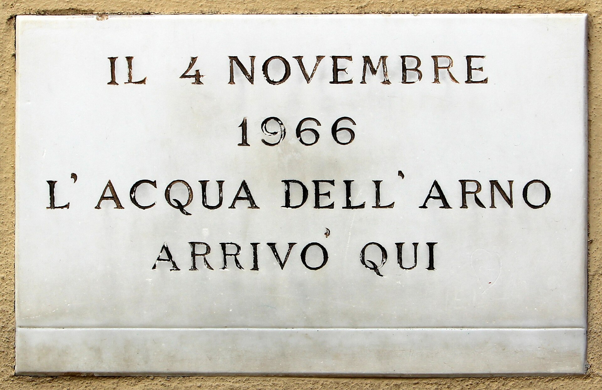 A white marble plaque set into a stone wall reading IL 4 NOVEMBRE 1966 L'ACQUA DELL'ARNO ARRIVO QUI