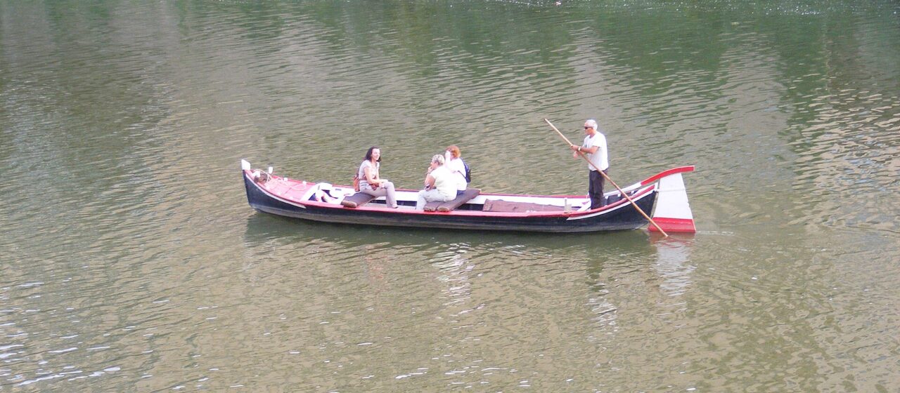 A traditional flat-bottomed barchetto with three passengers being poled along the green water of the Arno in Florence