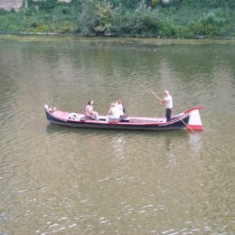 A traditional flat-bottomed barchetto with three passengers being poled along the green water of the Arno in Florence
