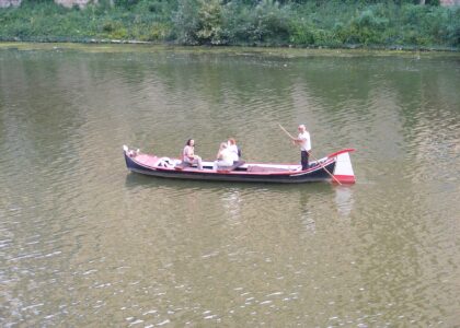 A traditional flat-bottomed barchetto with three passengers being poled along the green water of the Arno in Florence