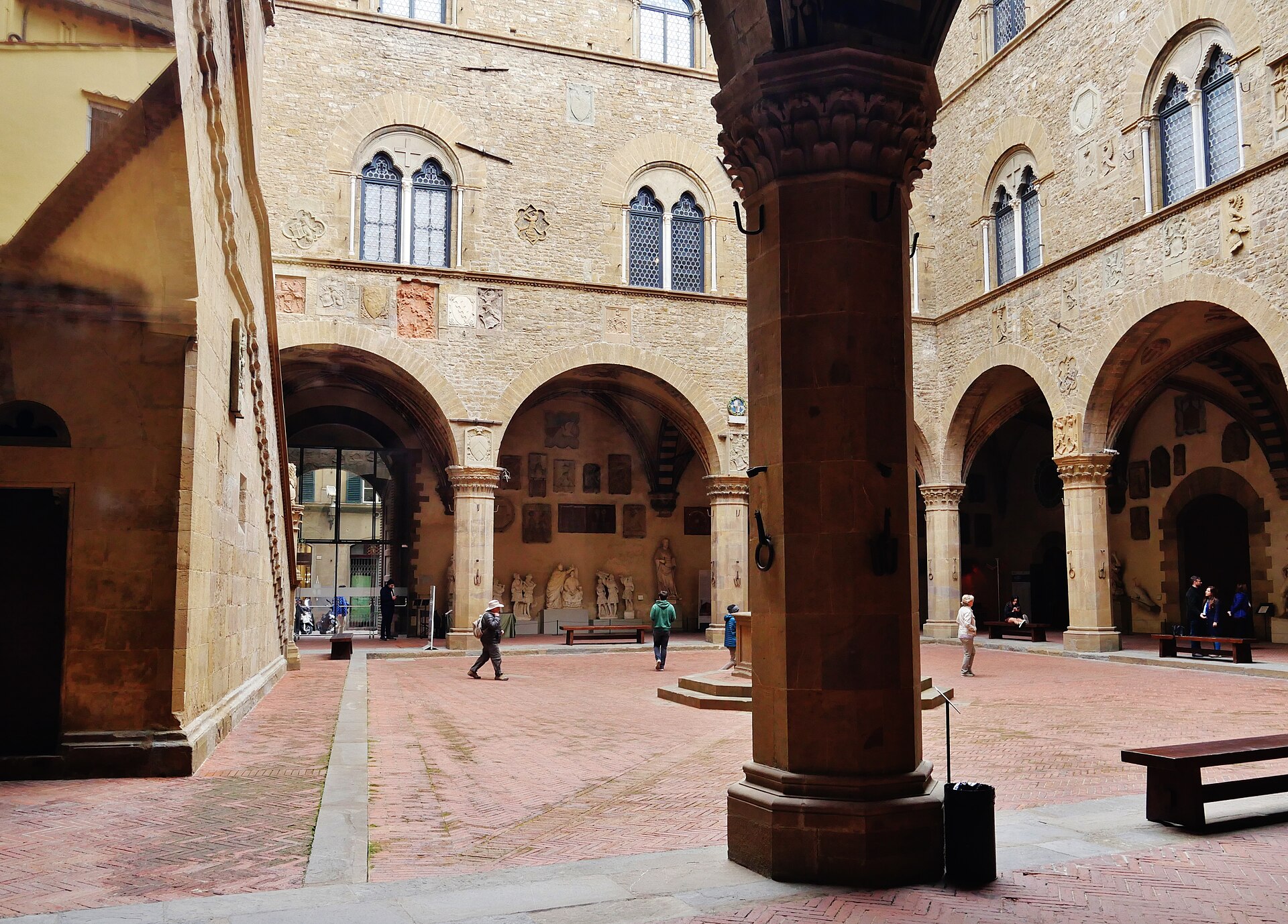 The arcaded medieval courtyard of the Bargello museum in Florence, with a handful of visitors in coats crossing the brick paving