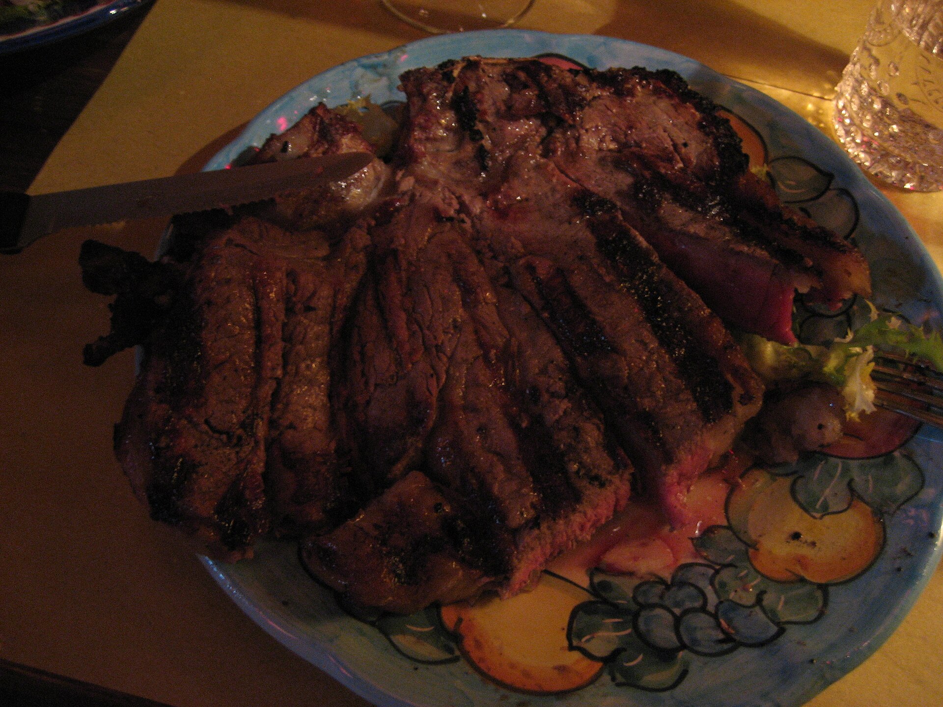 A carved bistecca alla fiorentina served on a decorated Tuscan plate with a knife alongside