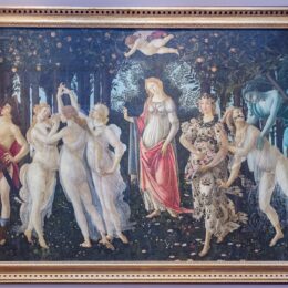 Botticelli's Primavera hanging in its gilt frame on a pale wall in the Uffizi Gallery
