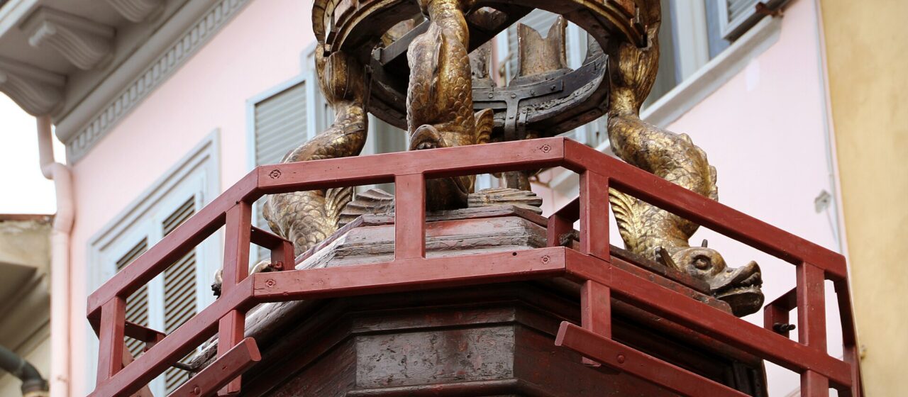 The gilded upper tier of the Brindellone cart, with carved dolphins supporting a crenellated golden crown above a red wooden railing