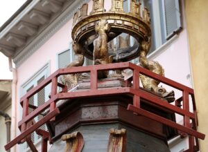 The gilded upper tier of the Brindellone cart, with carved dolphins supporting a crenellated golden crown above a red wooden railing