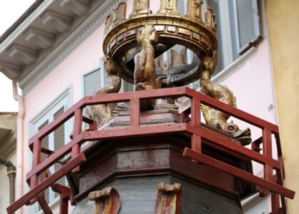 The gilded upper tier of the Brindellone cart, with carved dolphins supporting a crenellated golden crown above a red wooden railing