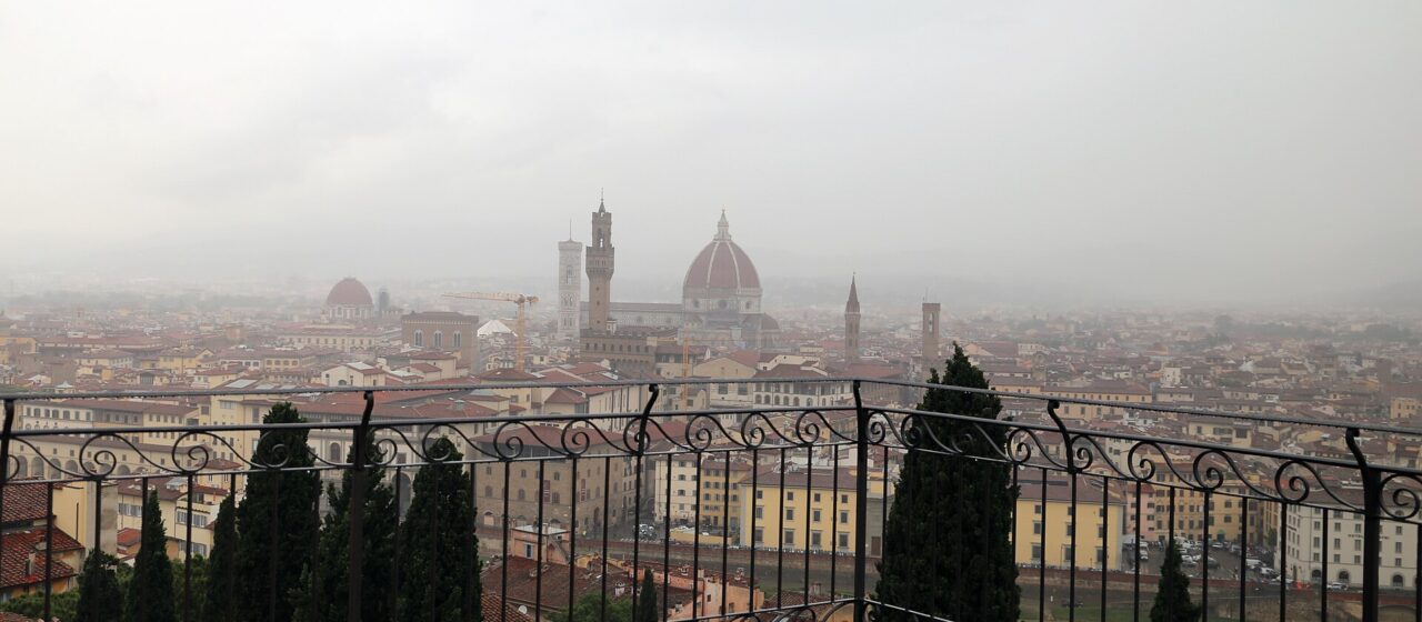 Florence seen through rain from the Villa Bardini terrace, the Duomo and Palazzo Vecchio tower half lost in grey murk above wet rooftops