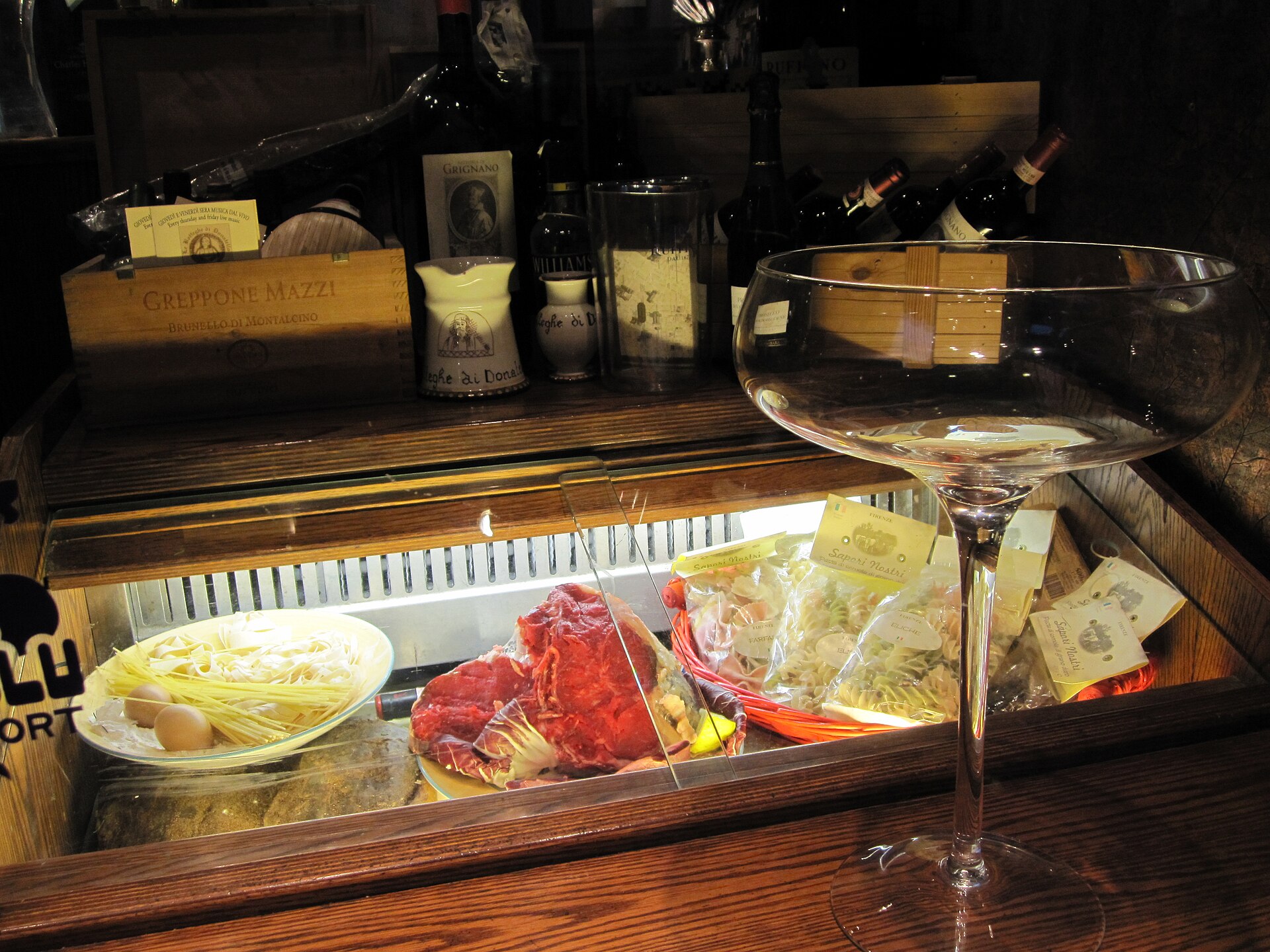 A restaurant display case in Florence showing a raw bistecca, fresh pasta and packets of dried pasta beneath bottles of Tuscan wine