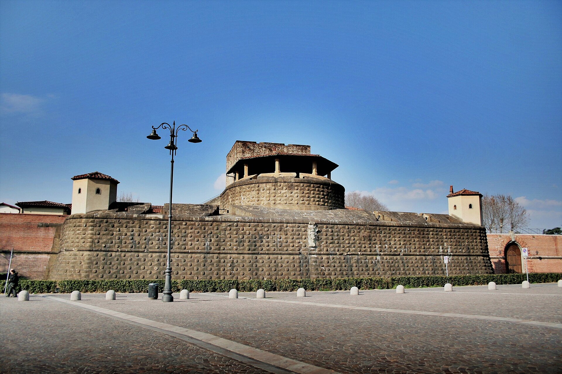 The stone bastion and brick curtain wall of the Fortezza da Basso in Florence under a clear blue winter sky