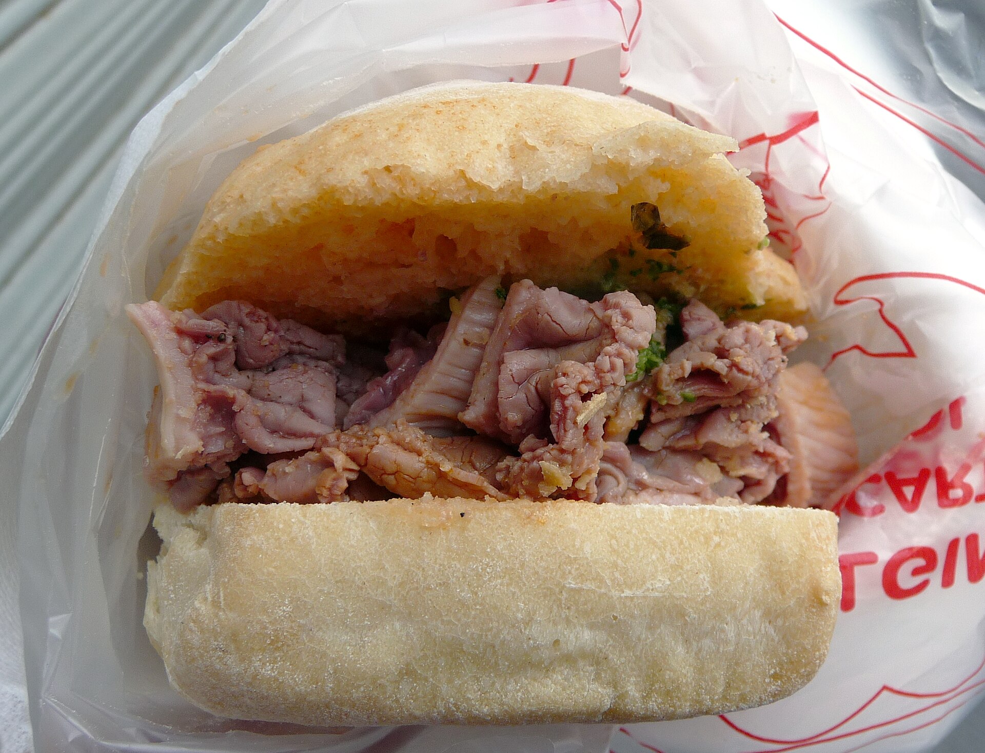 A lampredotto sandwich in a paper wrapper, filled with sliced tripe and green salsa verde