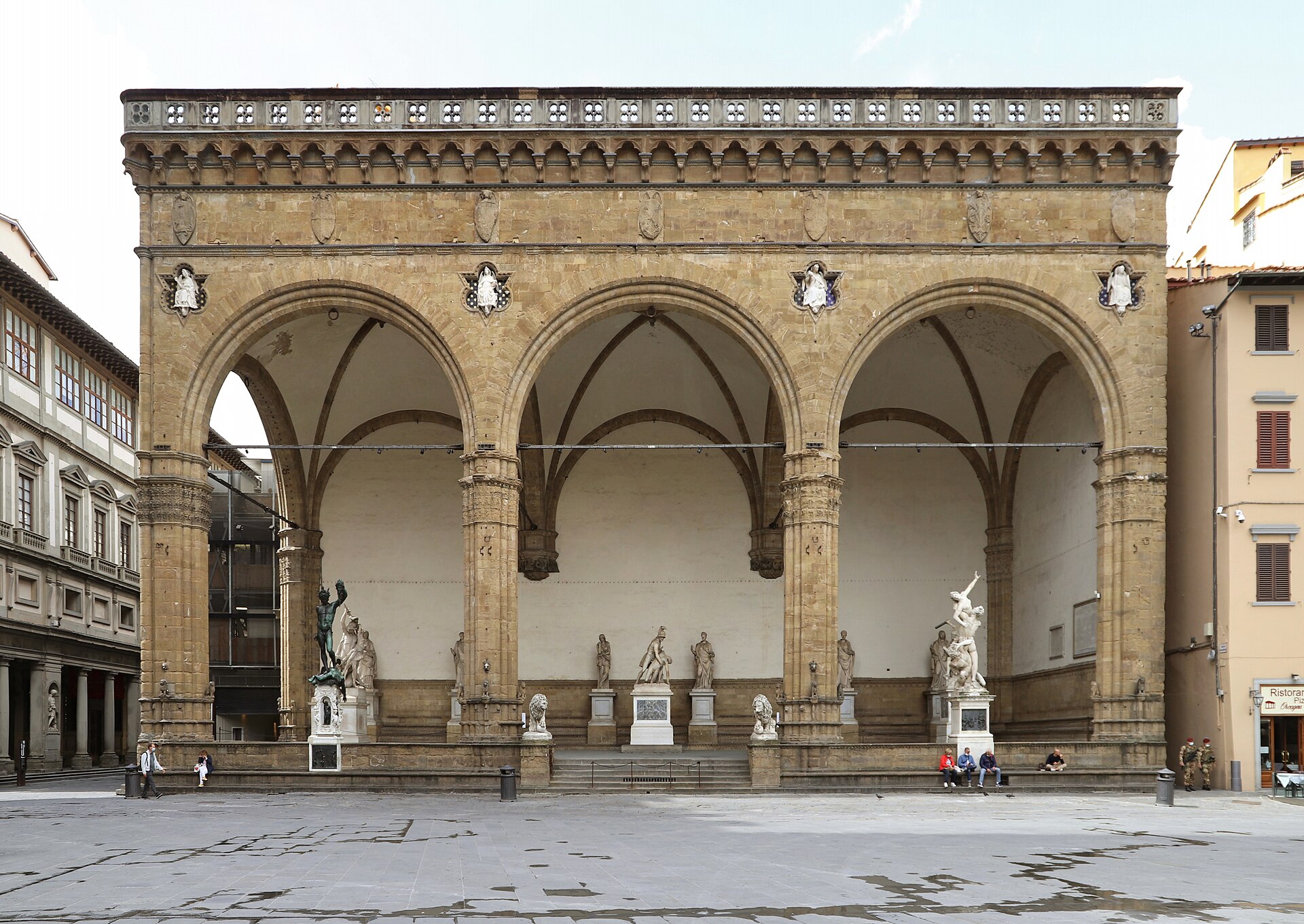 The three wide gothic arches of the Loggia dei Lanzi in Florence, filled with Renaissance statues, seen head-on from the piazza