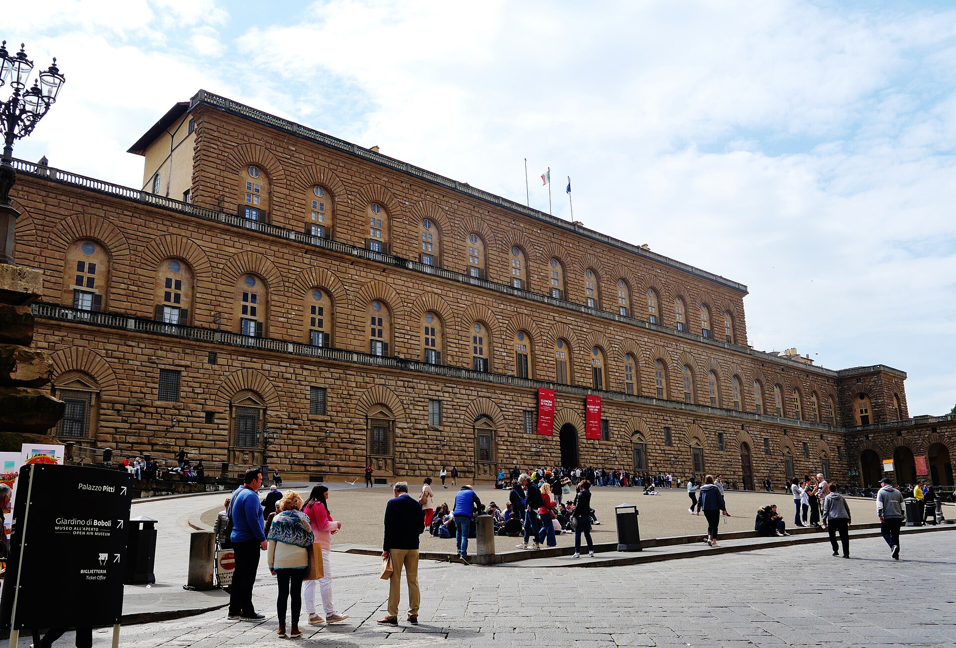 The long rusticated stone facade of Palazzo Pitti in Florence with visitors on the sloping forecourt