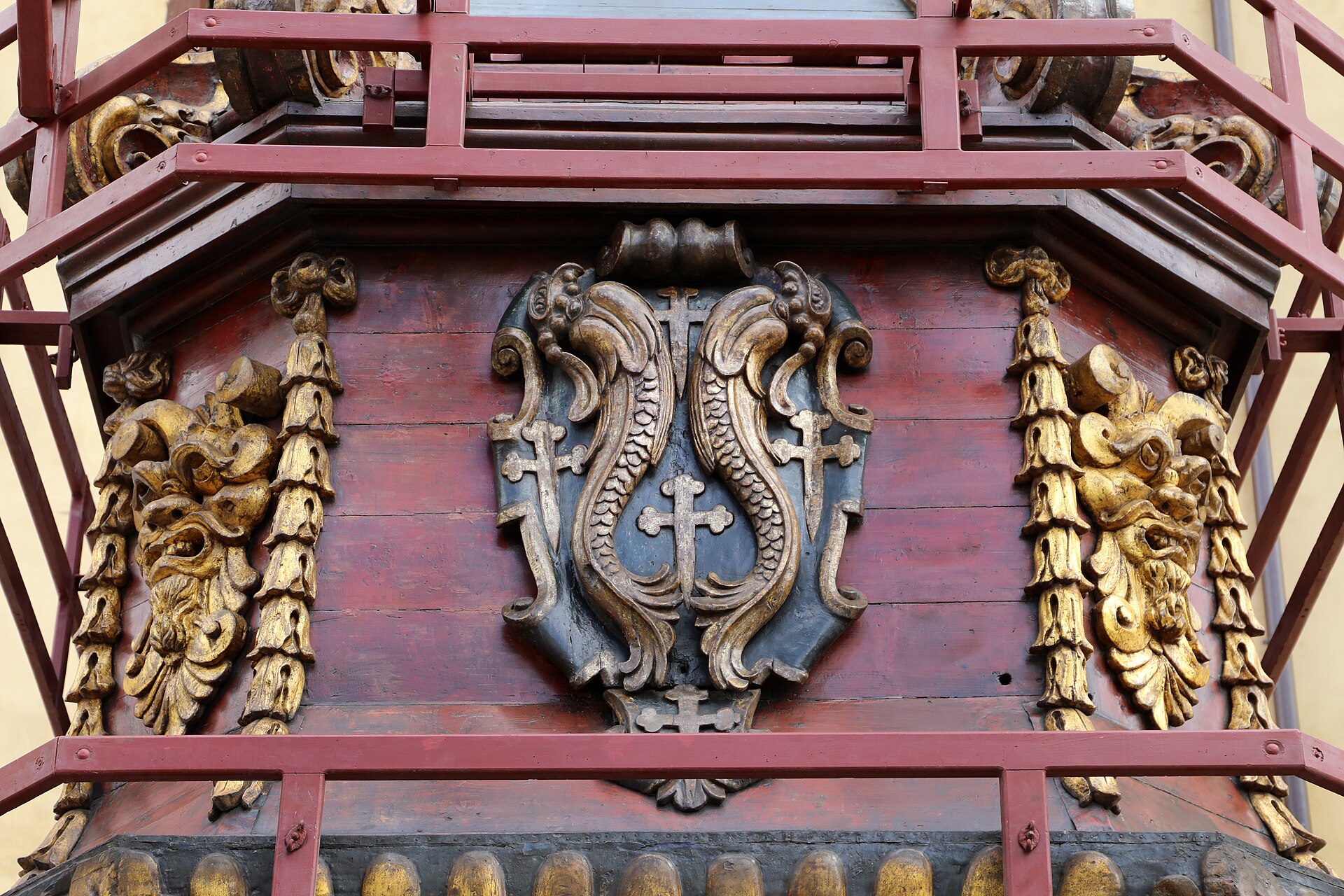 A carved and gilded coat of arms on the side of the Brindellone showing two facing dolphins and five crosses on a blue shield, flanked by grotesque masks