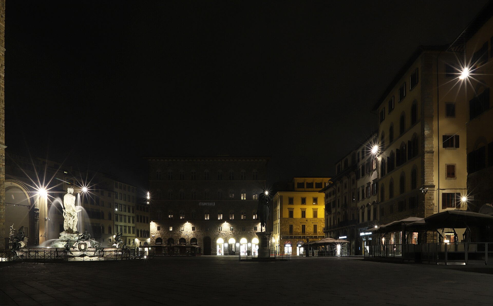 Piazza della Signoria in Florence at night, almost empty, with the floodlit Neptune fountain on the left and lit palazzi across the square