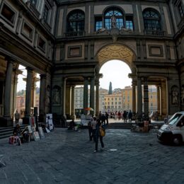 The long colonnaded courtyard of the Uffizi looking towards the arch that frames the Arno, with street artists and their easels along one side