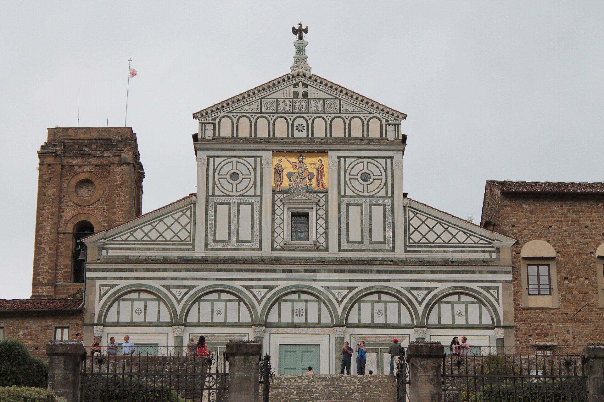 The green and white marble facade of San Miniato al Monte in Florence with visitors on the terrace below