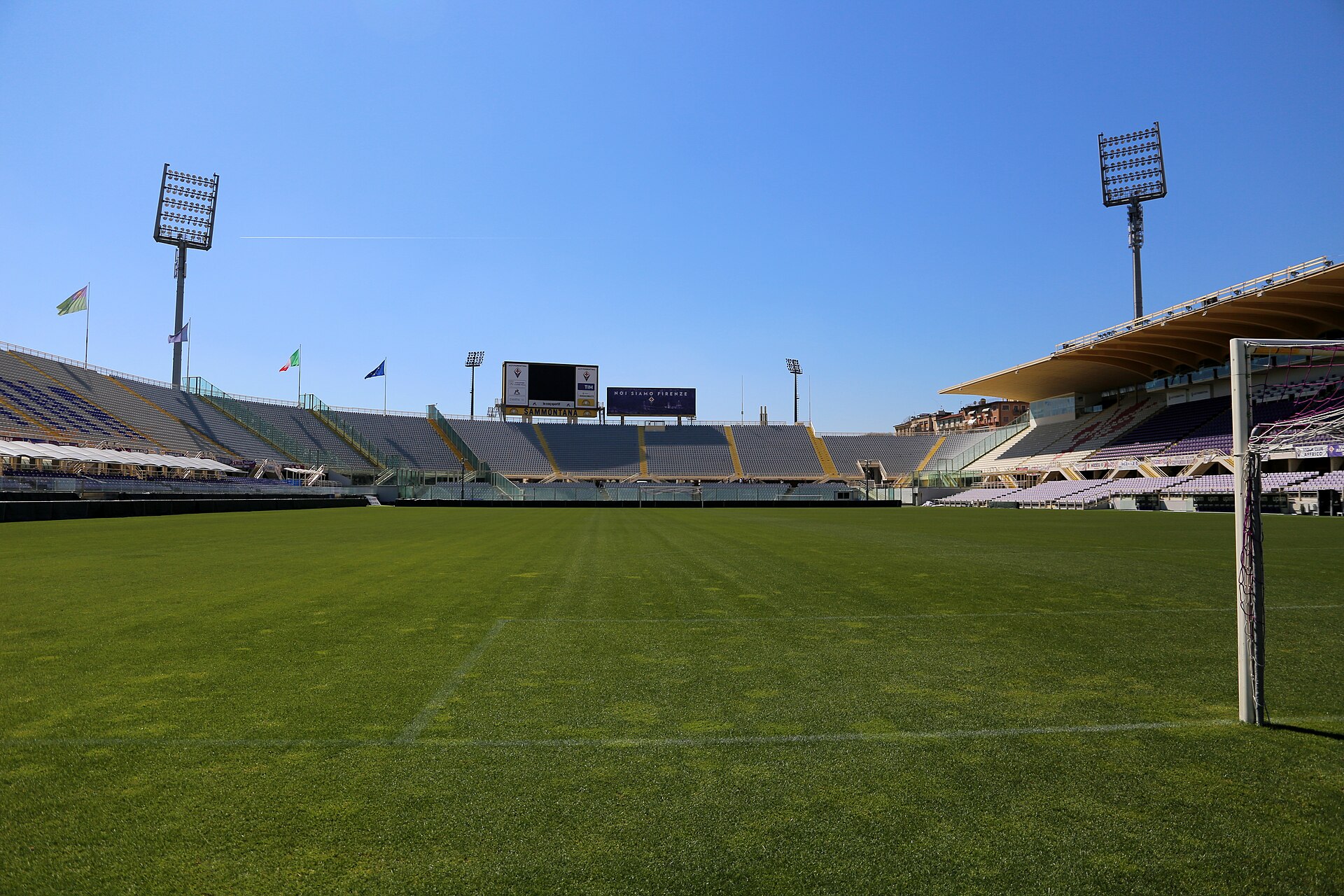 The empty pitch and purple seating of the Stadio Artemio Franchi in Florence under a blue sky
