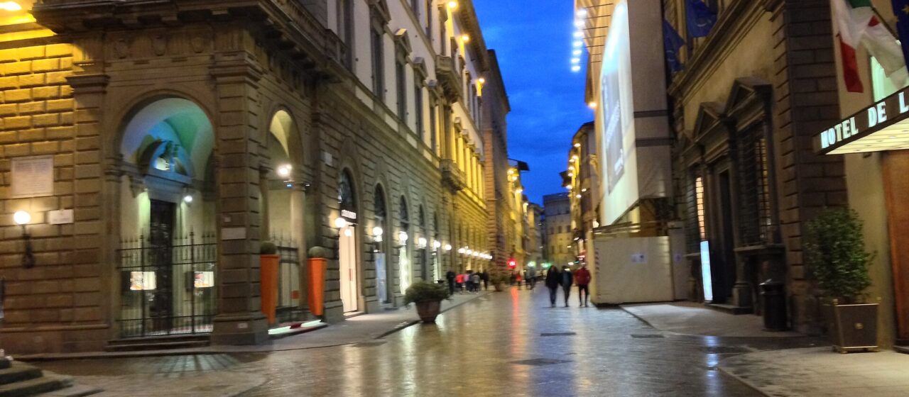 Via de' Tornabuoni in Florence at blue hour, wet paving reflecting shop lights, only a handful of people in the street