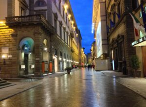 Via de' Tornabuoni in Florence at blue hour, wet paving reflecting shop lights, only a handful of people in the street