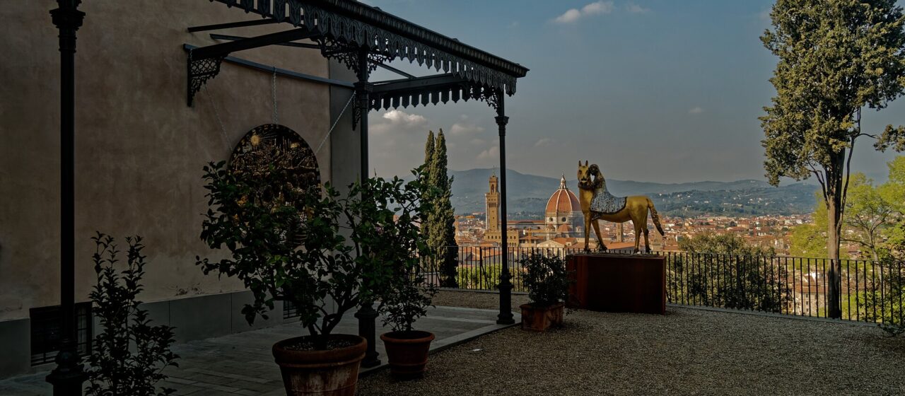 The terrace at Villa Bardini with an ornate ironwork canopy, potted lemon trees, a gilded horse sculpture and the Duomo and Palazzo Vecchio tower visible across the city below