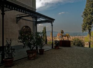 The terrace at Villa Bardini with an ornate ironwork canopy, potted lemon trees, a gilded horse sculpture and the Duomo and Palazzo Vecchio tower visible across the city below
