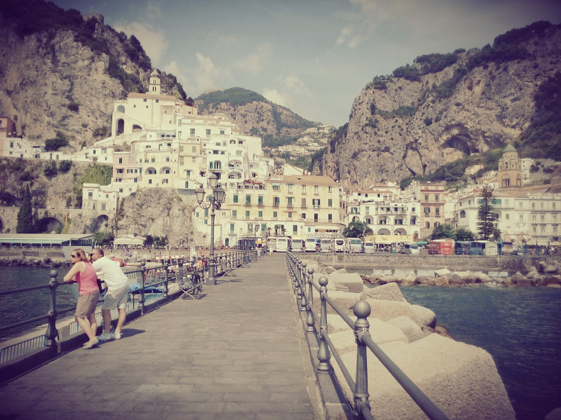 The town of Amalfi seen from the end of the ferry pier, white buildings and the cathedral bell tower rising up a steep valley between rocky mountainsides