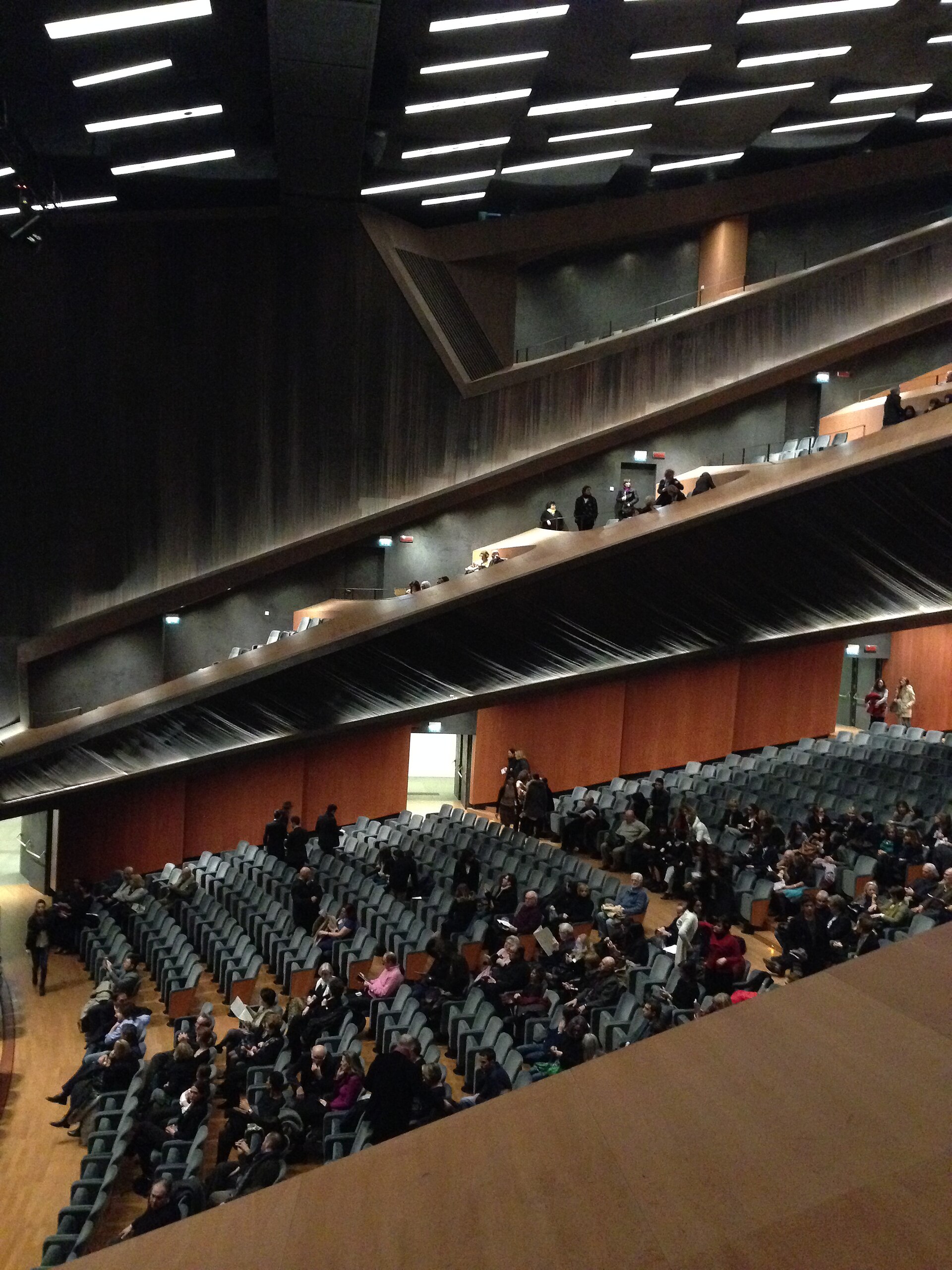 Audience members sit beneath stacked angular balconies inside the modern Teatro del Maggio Musicale Fiorentino in Florence.