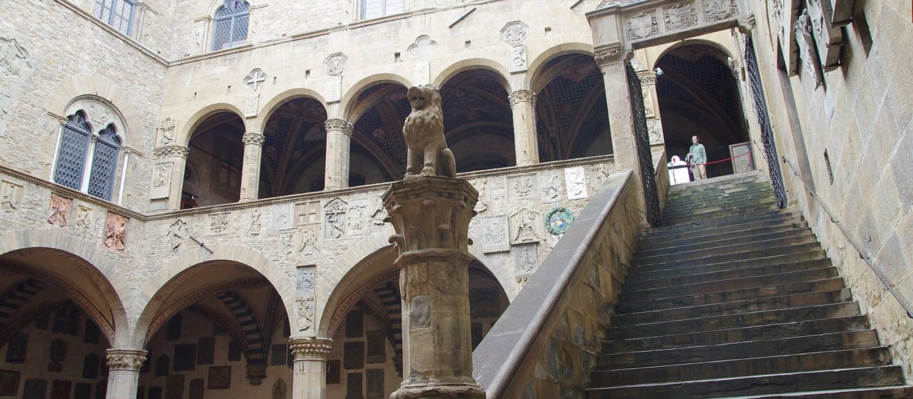 The Bargello courtyard in Florence has a broad outdoor staircase, two levels of arches and carved coats of arms.