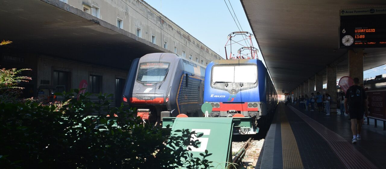 A blue locomotive and a modern regional train stand side by side at Florence Santa Maria Novella station.