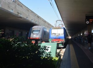 A blue locomotive and a modern regional train stand side by side at Florence Santa Maria Novella station.