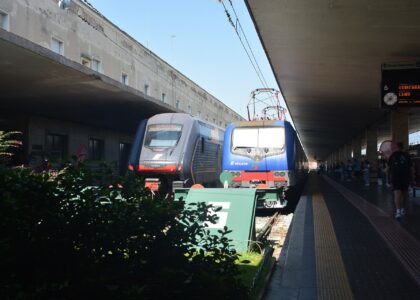 A blue locomotive and a modern regional train stand side by side at Florence Santa Maria Novella station.