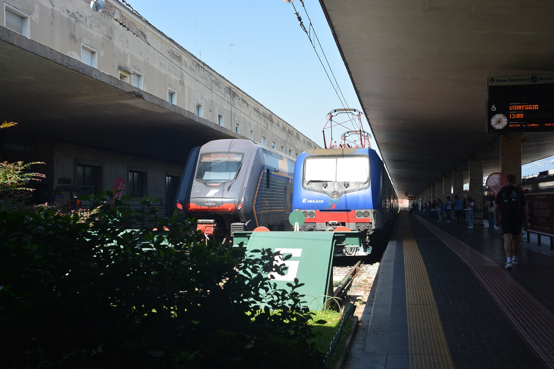 A blue locomotive and a modern regional train stand side by side at Florence Santa Maria Novella station.