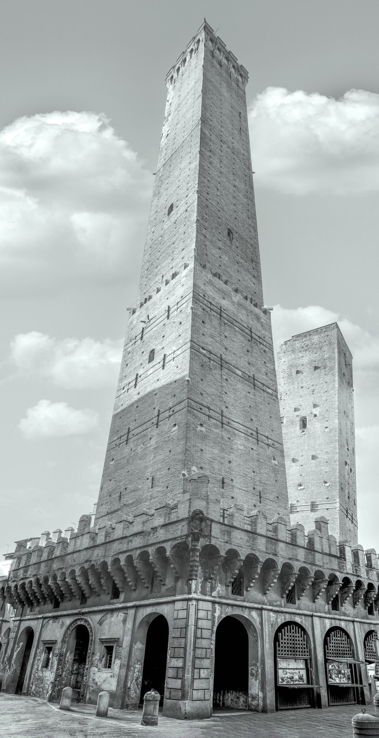 Bologna’s tall Asinelli tower rises above its arcaded base, with the shorter Garisenda tower behind, in black and white.