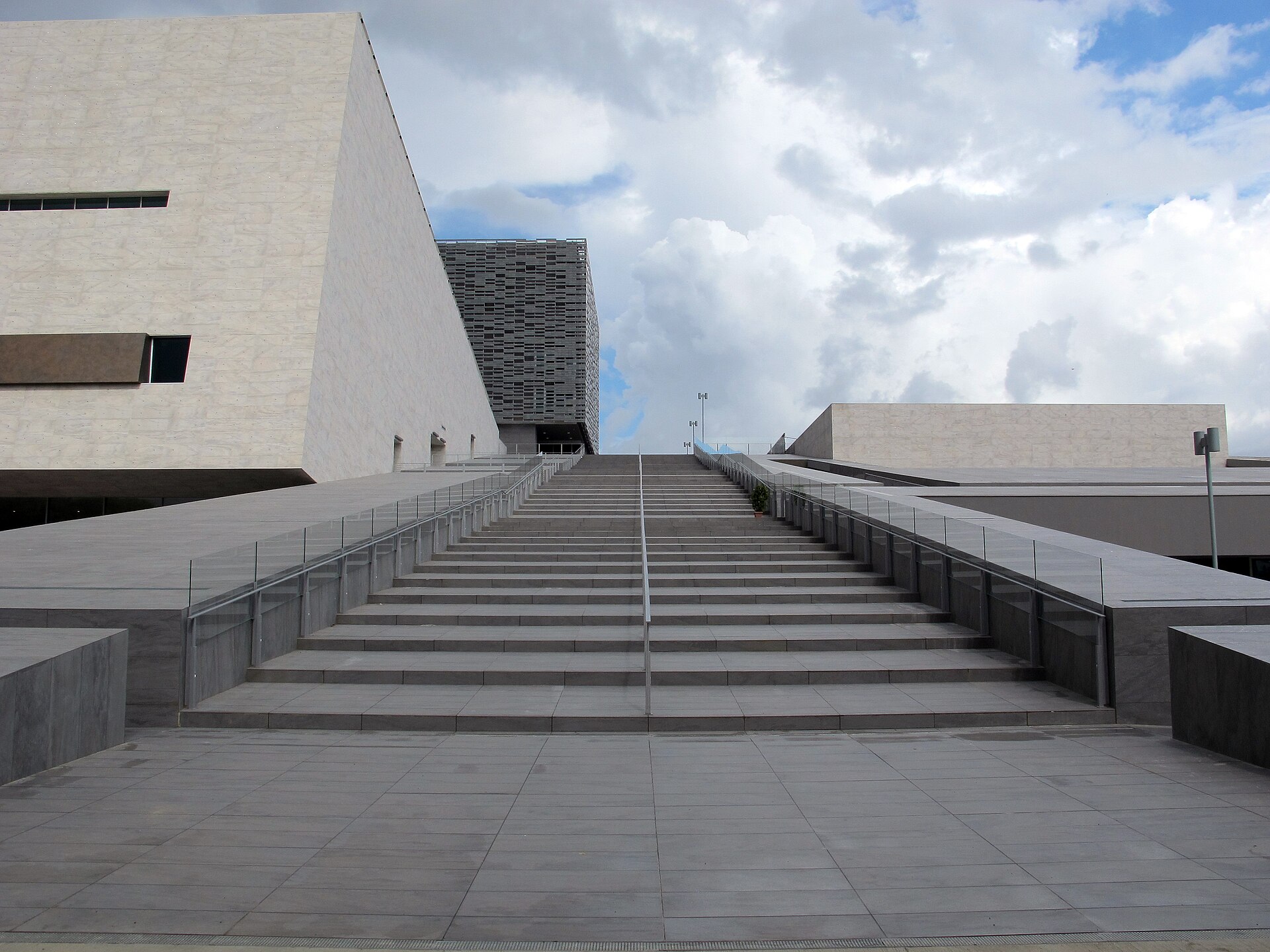 Broad outdoor stairs rise between railings beside the modern stone volumes of Florence's Teatro del Maggio Musicale Fiorentino.