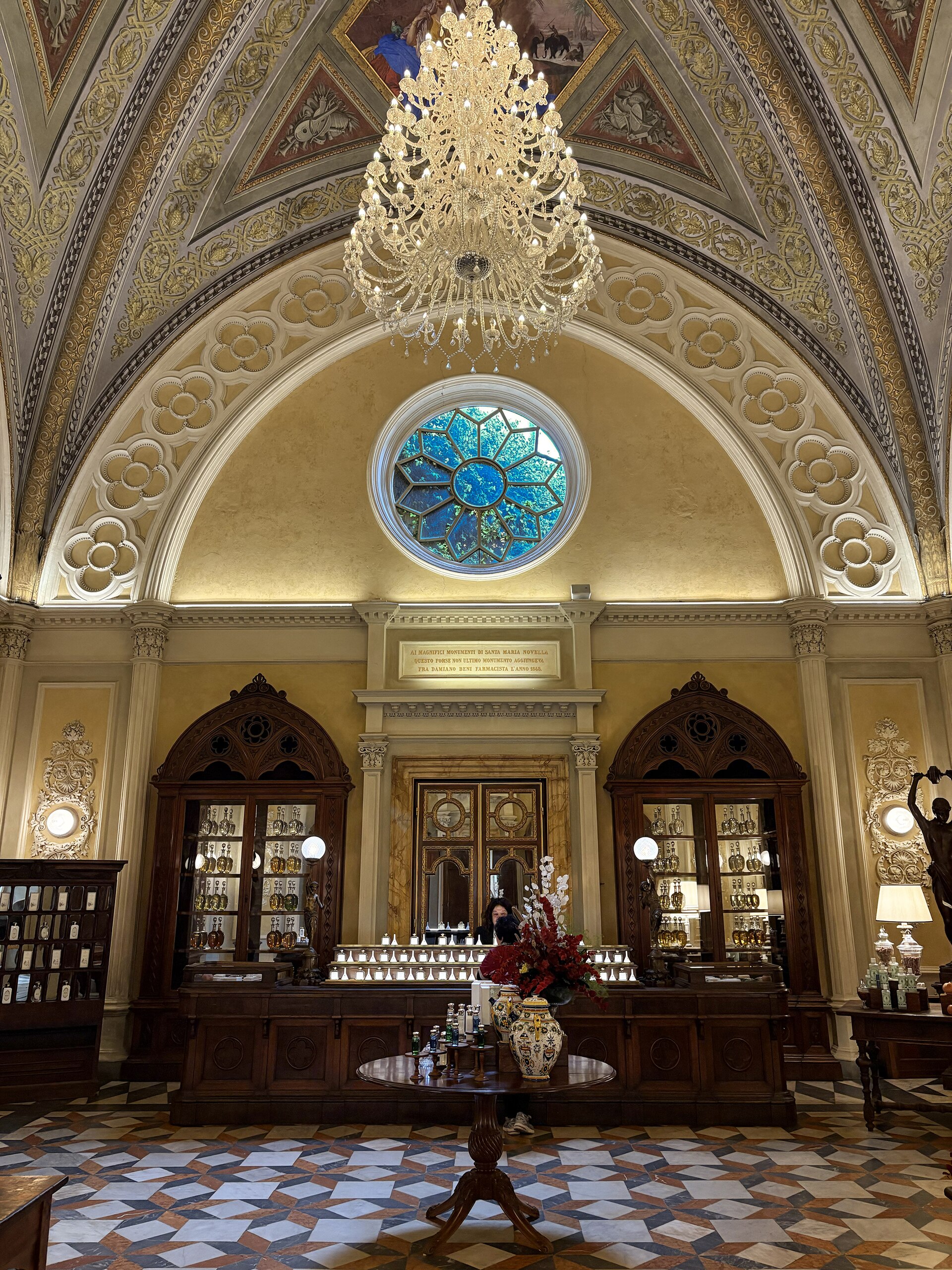 A chandelier hangs above wooden perfume counters beneath the decorated vault at Florence's Officina Santa Maria Novella.