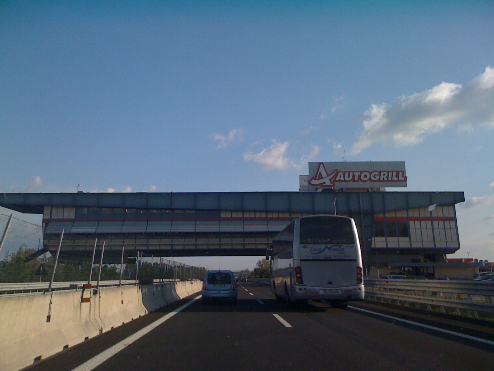A coach and car approach the overhead Autogrill building on the A1 motorway at Montepulciano between Florence and Rome.