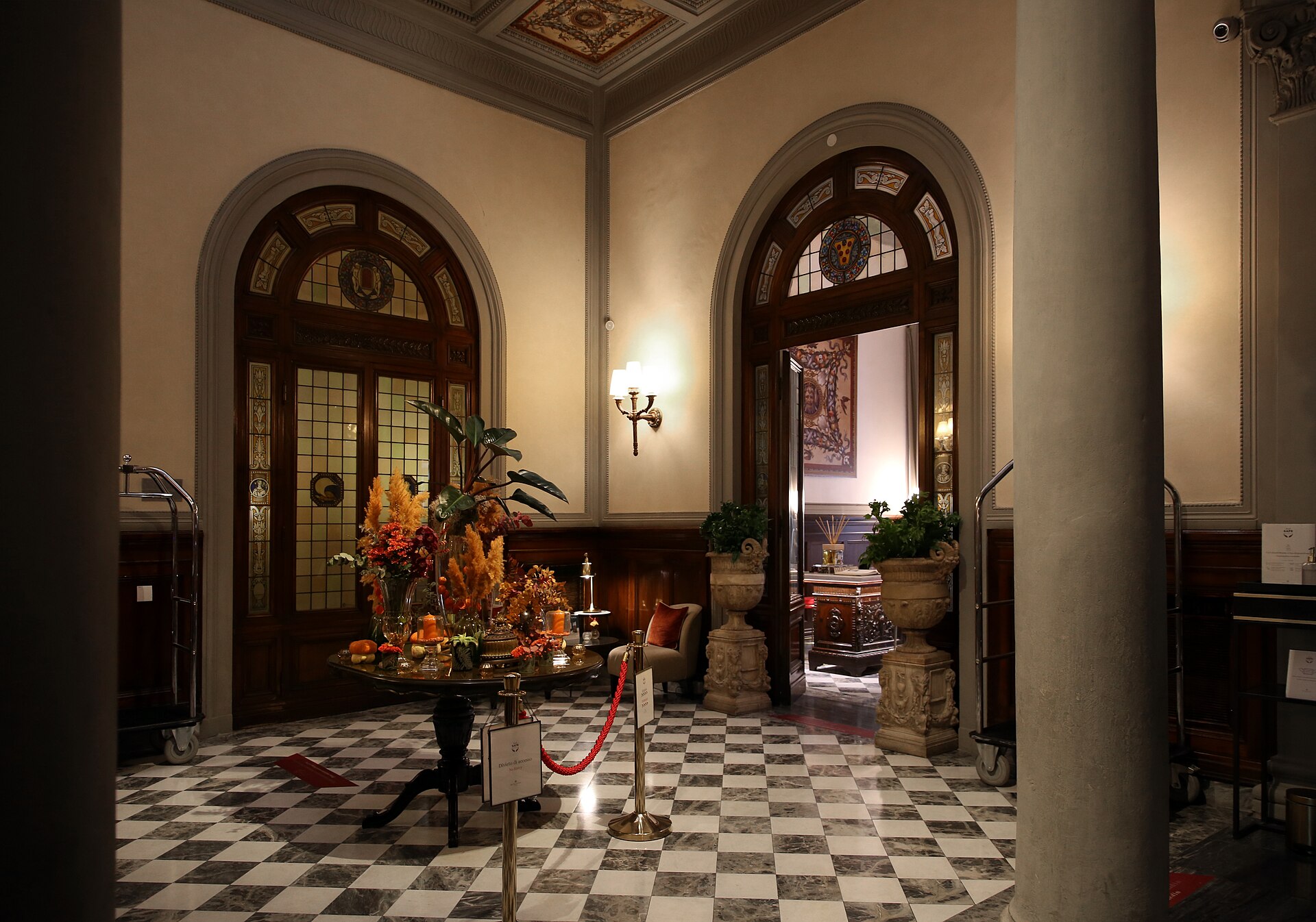 Columns and arched stained-glass doorways frame a checkerboard floor in Florence’s Hotel Porta Rossa hall.