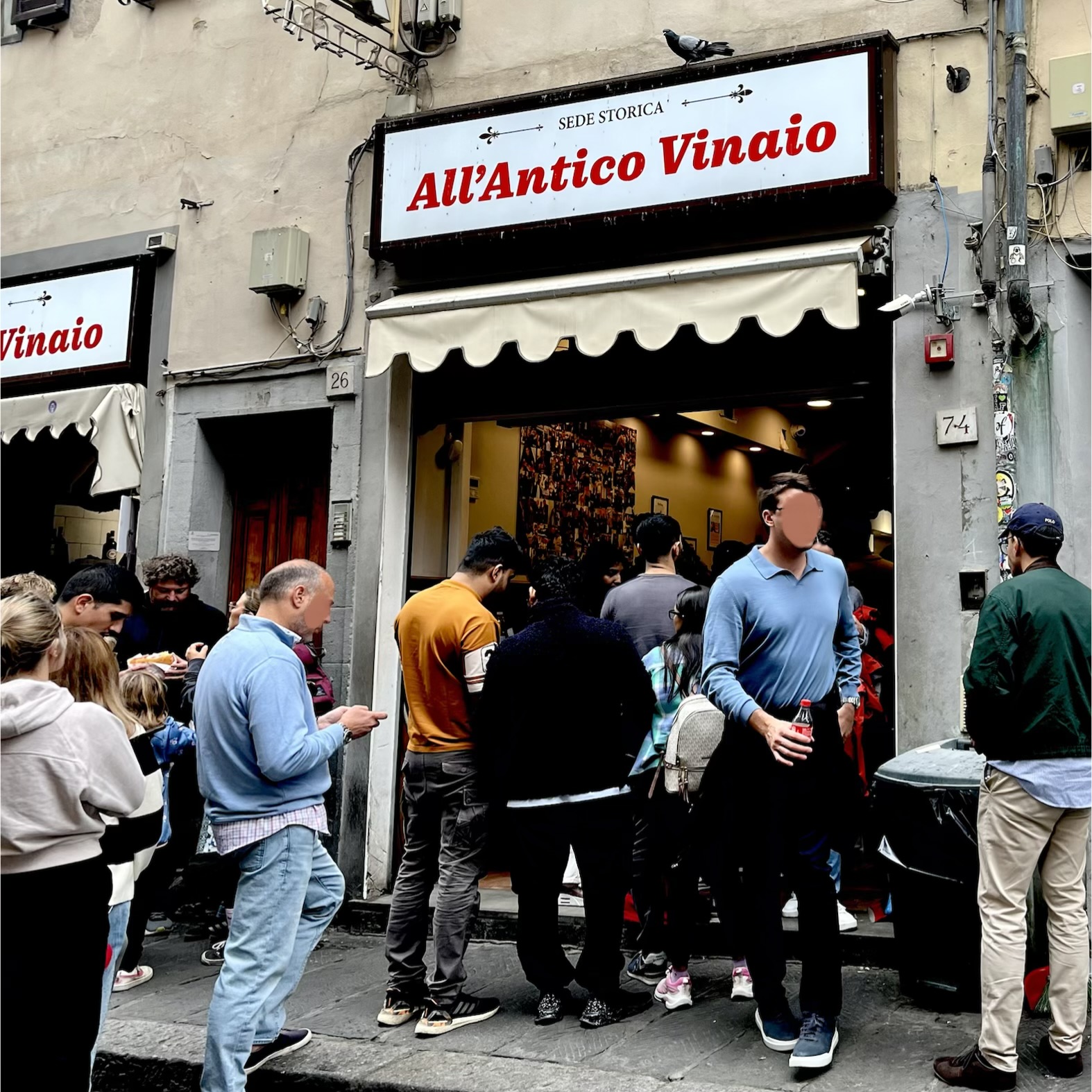 A crowd queues on a narrow Florence street at the open front of All'Antico Vinaio's historic shop, beneath its red-lettered white sign and awning.