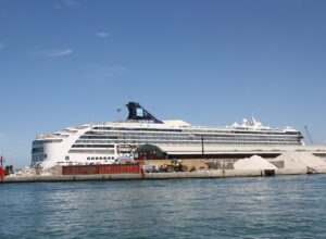 A large white cruise ship moored inside the breakwater of Livorno harbour, with a red harbour light and piles of quarried stone on the quay in front