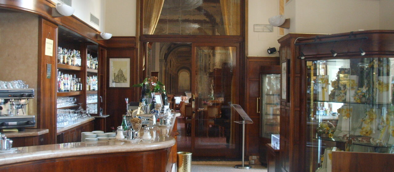 A curved wood-and-marble counter, espresso machine, bottles and glassware fill the historic interior of Caffe Paszkowski in Florence.