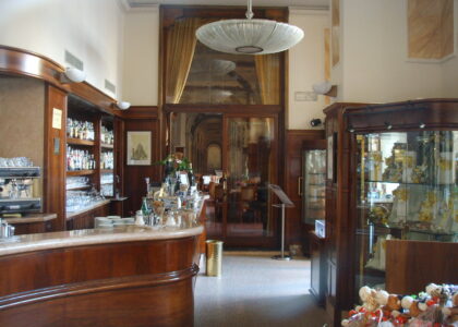 A curved wood-and-marble counter, espresso machine, bottles and glassware fill the historic interior of Caffe Paszkowski in Florence.