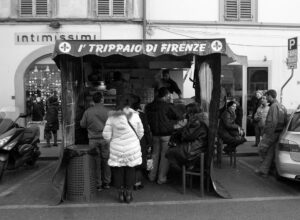 Customers gather at a lampredotto kiosk beneath the I' Trippaio di Firenze awning on Florence's Via Gioberti.