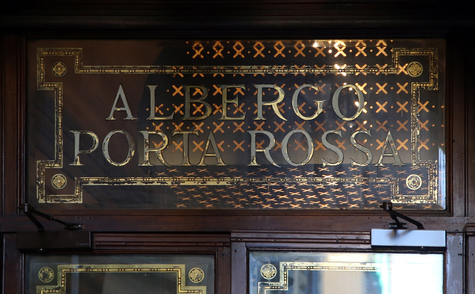 Decorated glass spelling Albergo Porta Rossa sits above dark wooden entrance doors at the historic Florence hotel.