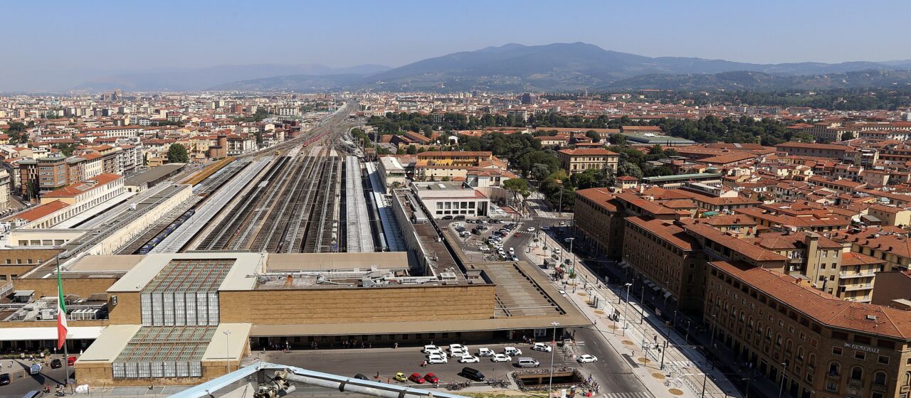 Florence Santa Maria Novella station seen from above, with its stone facade, taxi forecourt and long platform roofs.