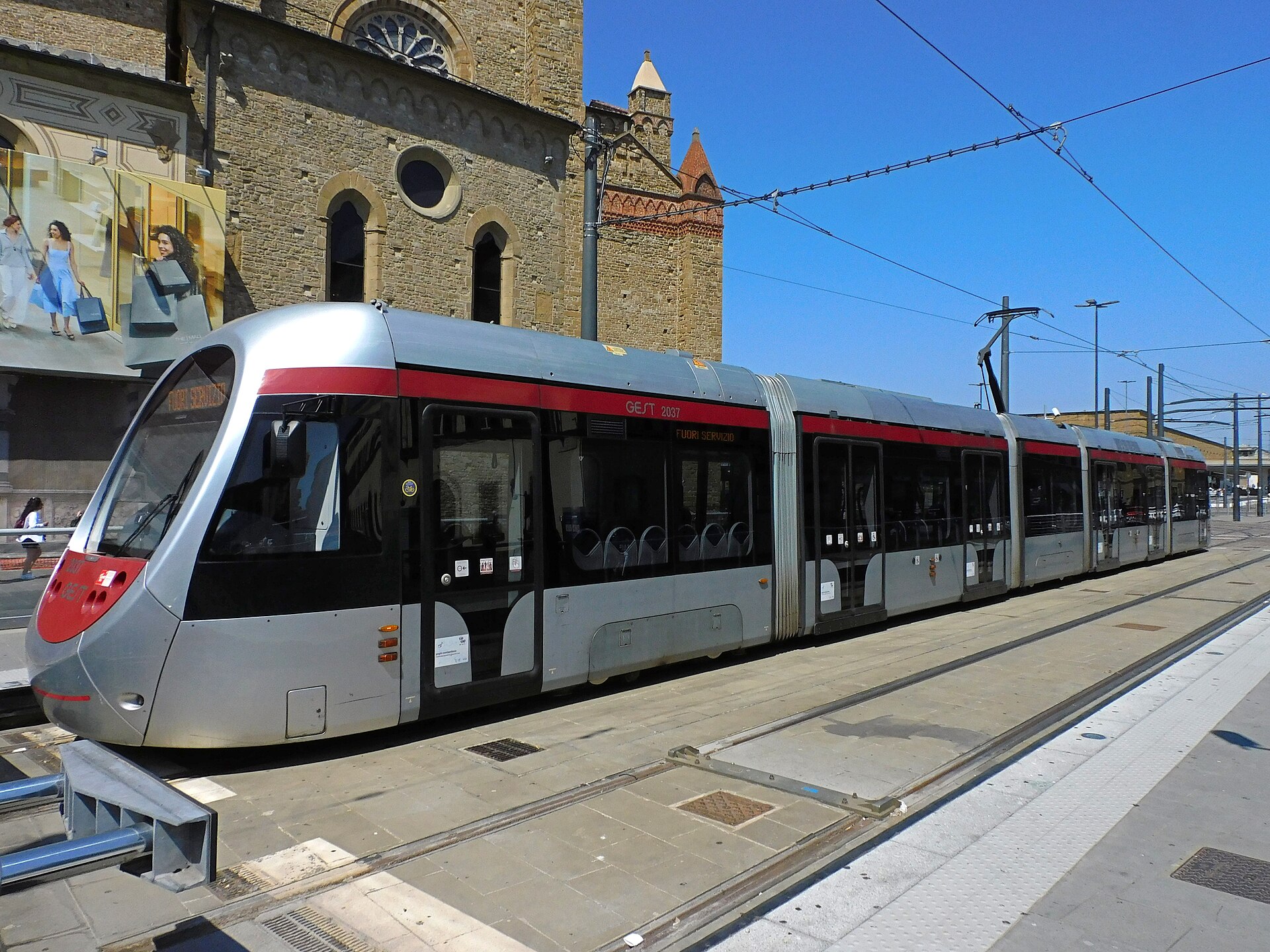 A Florence tram stands at Unità stop beside the stone walls of Santa Maria Novella and paved platforms.