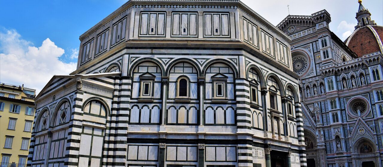 Florence's octagonal Baptistery displays geometric green and white marble walls, with the cathedral facade and dome rising behind visitors in the square.