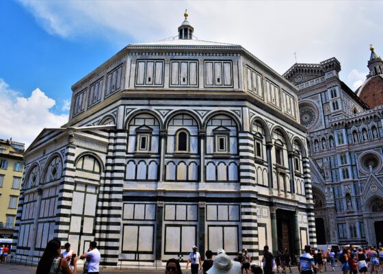 Florence's octagonal Baptistery displays geometric green and white marble walls, with the cathedral facade and dome rising behind visitors in the square.