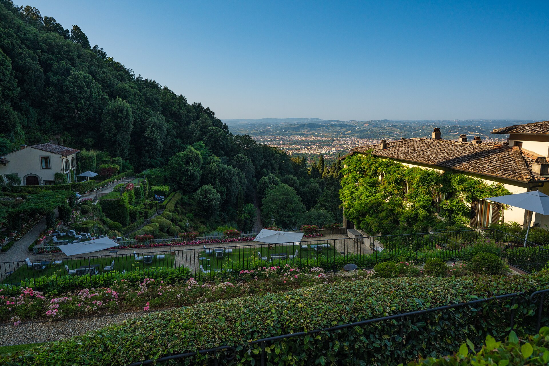 Flower beds and ivy-covered buildings at Villa San Michele in Fiesole overlook Florence across a wooded hillside.